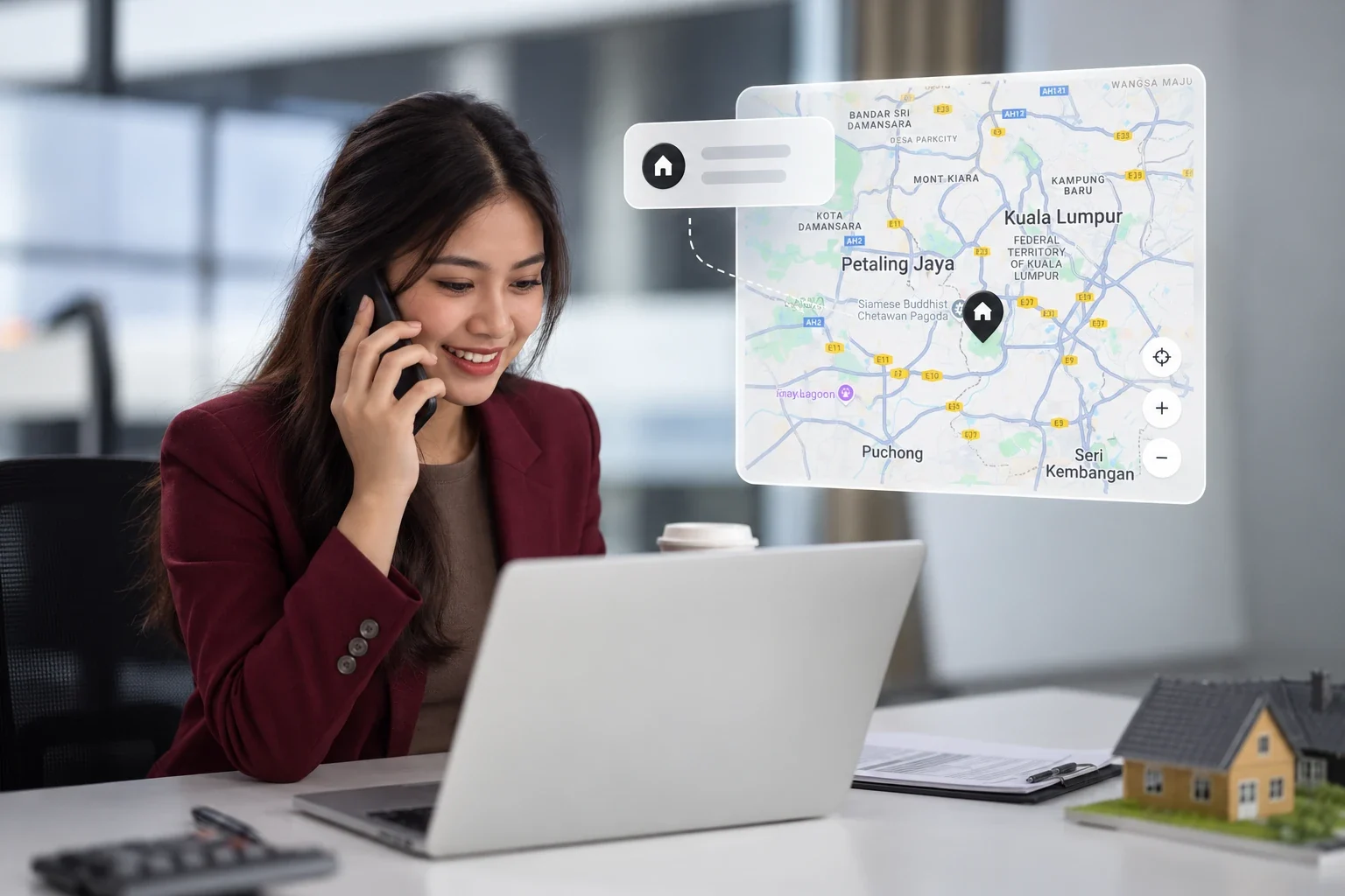 A property agent on the phone at her laptop, beside a map of Kuala Lumpur and Petaling Jaya with a pinned property.